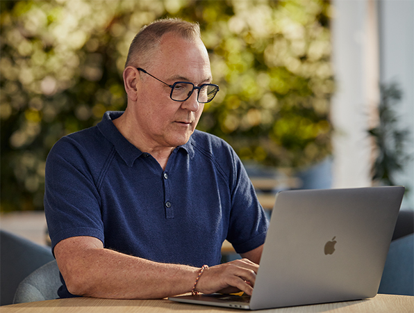 Empleado de Software y servicios de Apple trabaja en el exterior en una MacBook con áreas verdes al fondo.