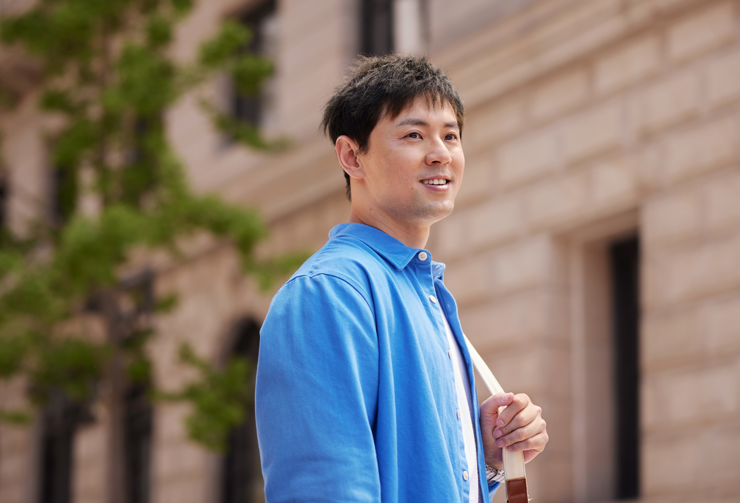 벽돌 사무실 건물 앞에서 어깨에 가방을 메고 미소 짓고 있는 Apple 직원.