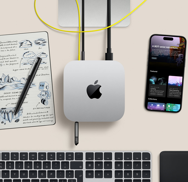 Vista desde arriba de un Mac mini sobre un escritorio con cables y un flash drive conectados en los puertos. Junto al Mac mini hay un teclado inalámbrico, un trackpad, un iPhone y un block de notas.