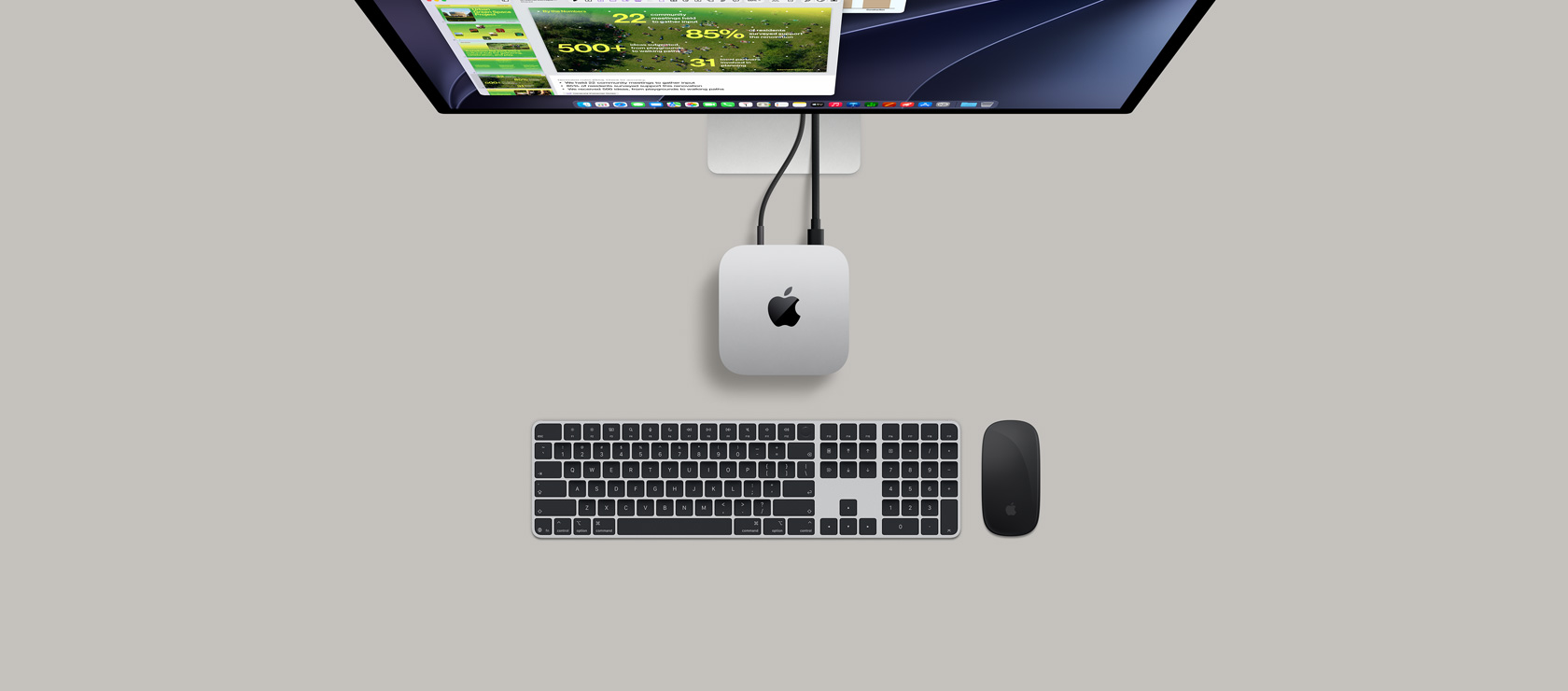 Pohled shora na stříbrný Mac mini připojený k monitoru, na kterém je rozehraná hra, vedle jsou bezdrátová klávesnice, herní ovladač a modré AirPody Max