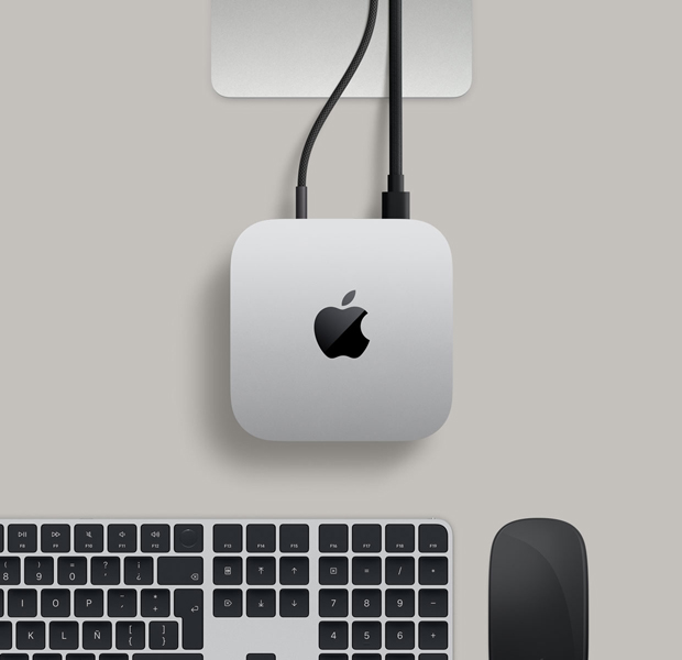 Vista desde arriba de una Mac mini color plata en un escritorio con un disco externo conectado, junto a un Magic Keyboard color plata y blanco, un Magic Mouse blanco y una cámara