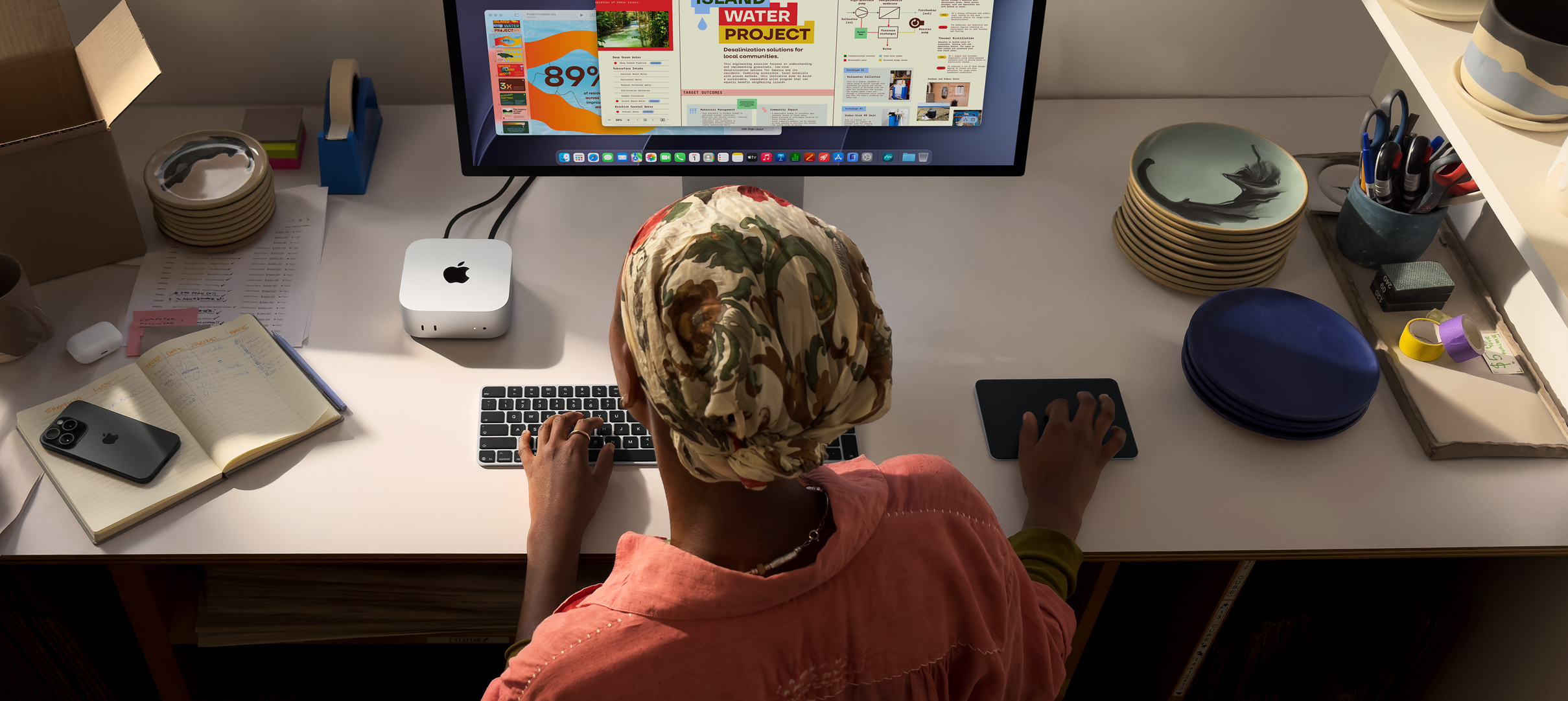 Masada oturan ve Mac mini kullanan bir kişinin ekranında renkli uygulamalar görülüyor
