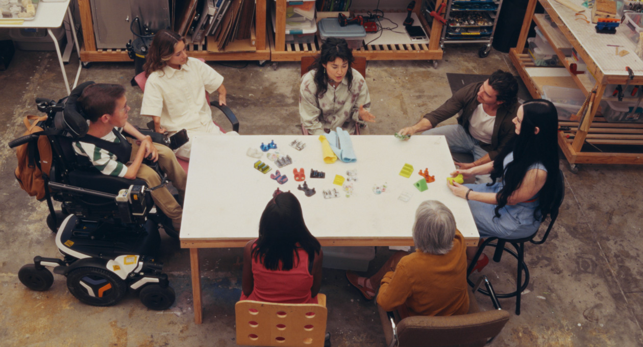 Un groupe de personnes ayant divers besoins en matière de motricité, assis à une table, qui regardent différents accessoires adaptés et colorés pour téléphones intelligents