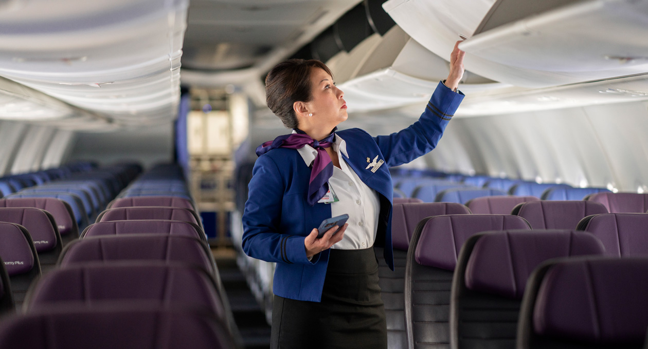 Une agente de bord tient un iPhone en ouvrant un compartiment supérieur dans un avion vide