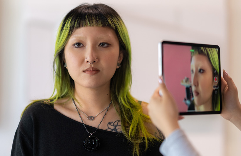 Una estudiante usa la cámara de un iPad para escanear el rostro de otra estudiante con el cabello teñido de verde.