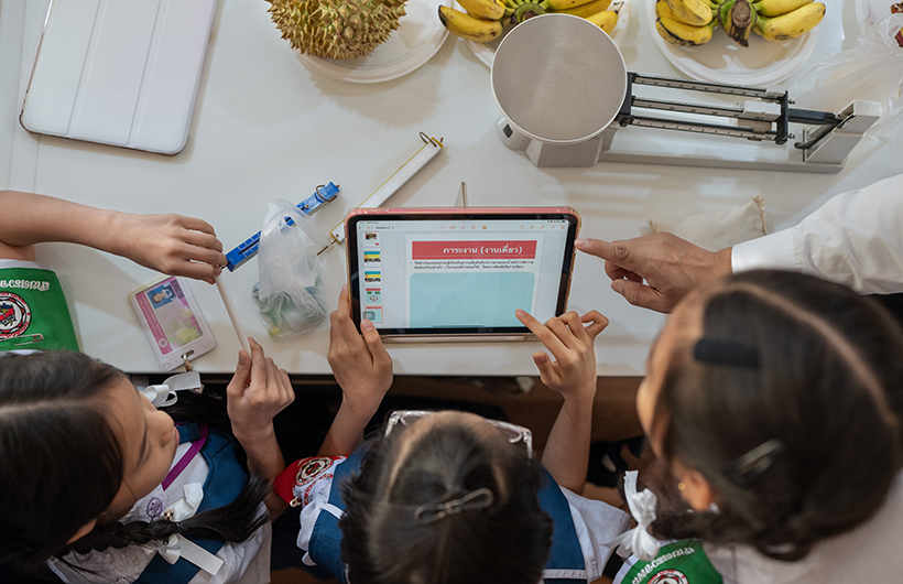 Tres estudiantes de primaria alrededor de un iPad colaborando en una presentación de un proyecto de ciencias.
