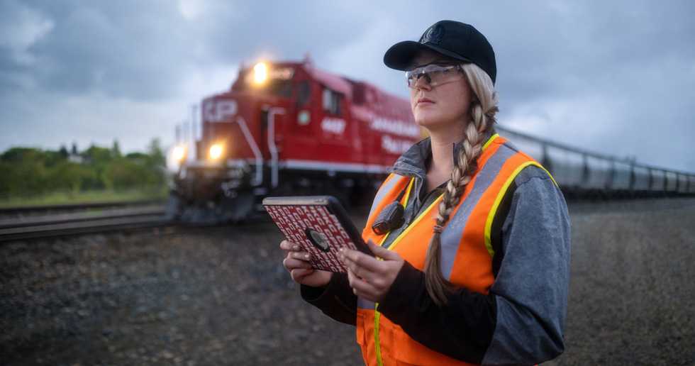 Una trabajadora ferroviaria sostiene un iPad y mira las vías mientras pasa un tren