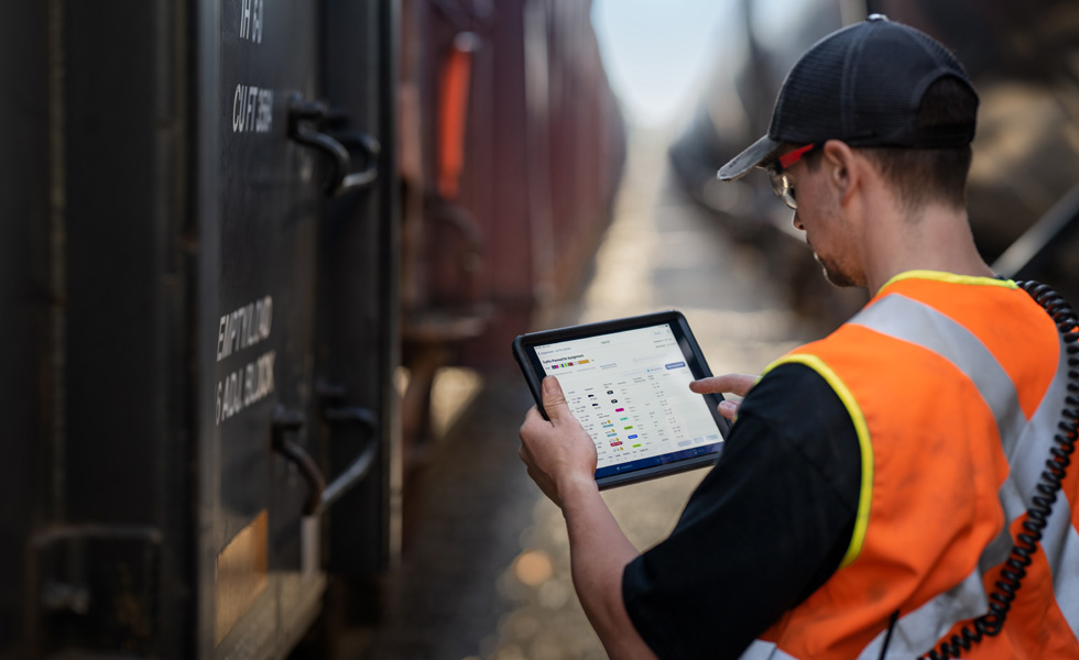 Un impiegato ferroviario è in piedi accanto a un treno e sta consultando un iPad su cui sono mostrate informazioni sulla pianificazione