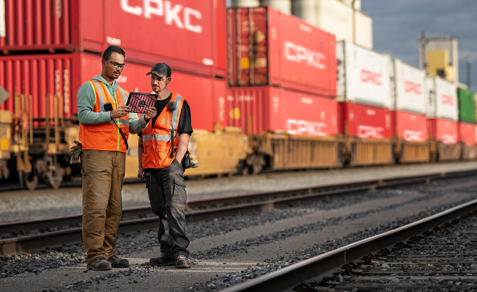 Due impiegati ferroviari consultano un iPad mentre si trovano vicino a un treno fermo che trasporta container