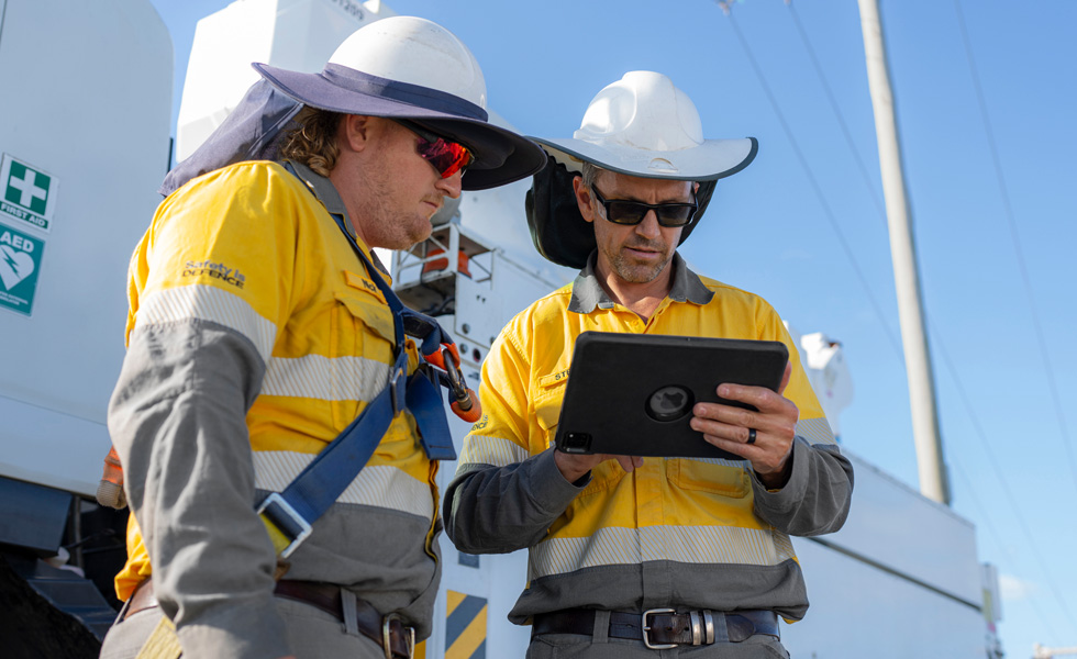 Duas pessoas da equipe de campo colaboram em um iPad ao lado de um veículo da empresa