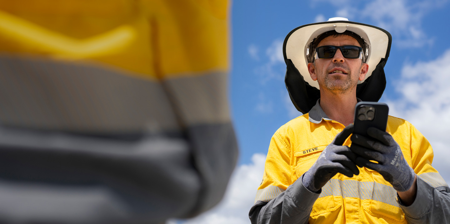 Uma pessoa da equipe de campo vestindo equipamento de proteção segura um iPhone enquanto conversa com alguém