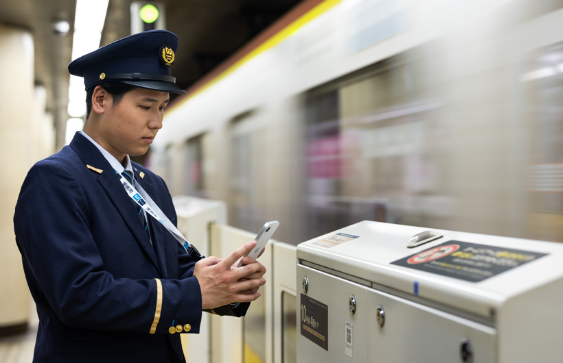Un addetto della stazione in piedi sul binario che usa l’iPhone per scansionare un codice QR mentre un treno passa.