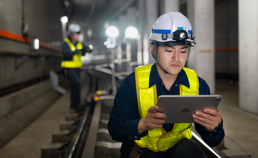 Un operaio con giubbotto di sicurezza e casco che guarda un iPad mentre esegue la manutenzione nelle gallerie della metropolitana di Tokyo.