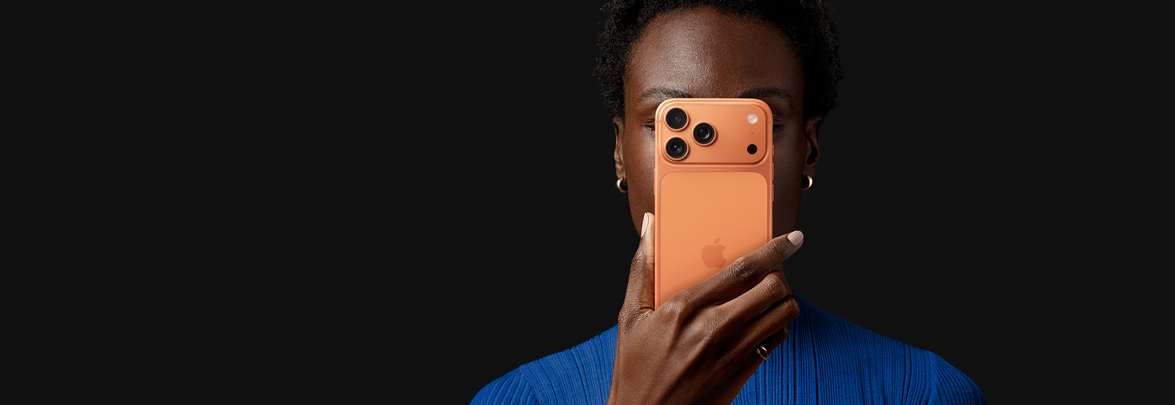 Personne tenant un iPhone 17 Pro devant son visage, dont on voit la face arrière, couleur orange cosmique