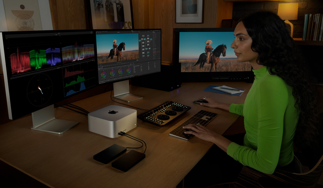 Una persona che esegue un montaggio video su un Mac Studio collegato a tre monitor