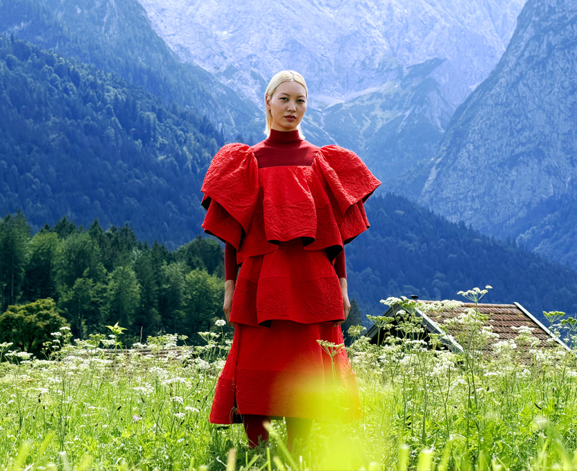 A model in a bright red dress stands in a mountain valley, showcasing the wide colour gamut of Studio Display XDR