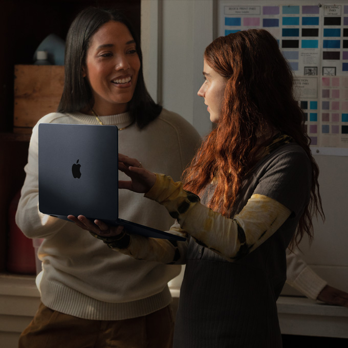 Une prof et une élève discutent en tenant un MacBook